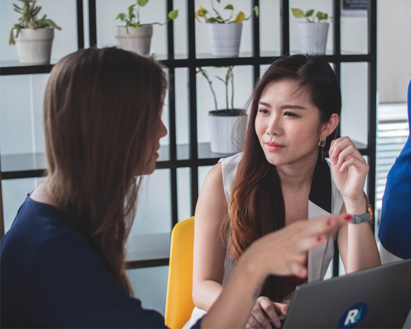 Corporate Event Planner - Two Women Talking In Office Space